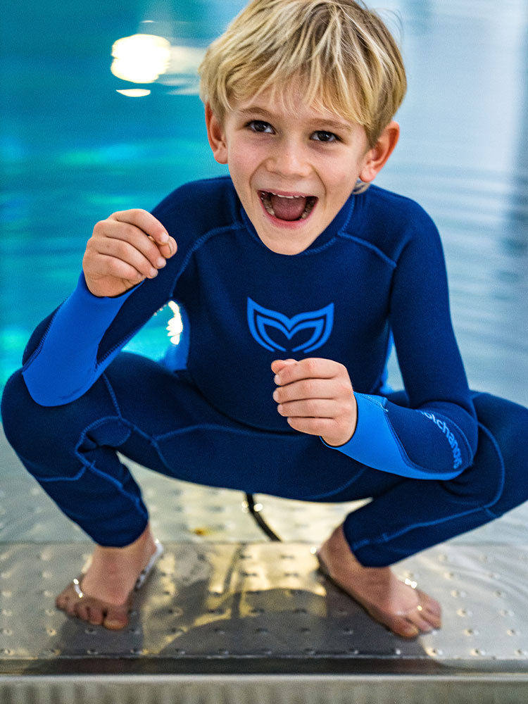 A boy crouching beside a pool wearing a blue Molchanovs childrens wetsuit
