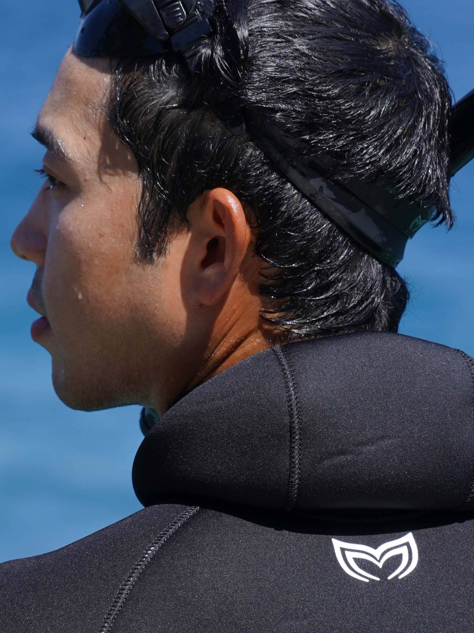 A shot from behind of a diver wearing a black double lined wesuit with the hood down.