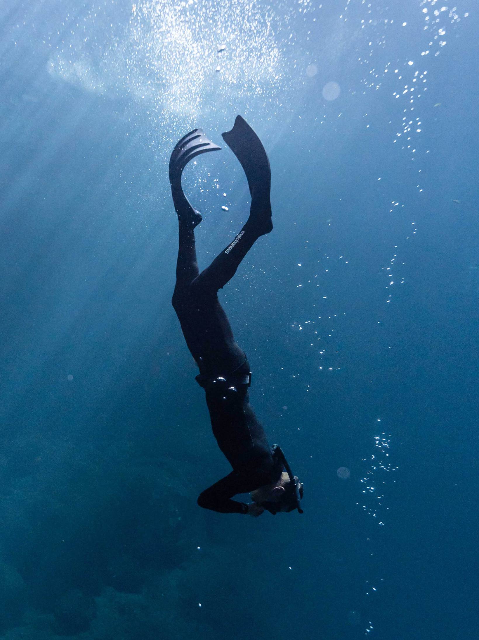 A diver descending wearing a black two piece double lined wetsuit.