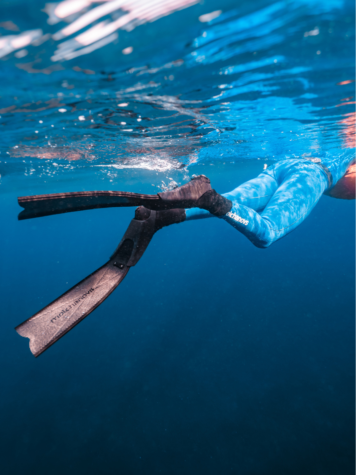 Freediver near the surface wearing Molchanovs SPORT Bifins 3 Carbon fiber fins and a blue wetsuit, underwater action shot