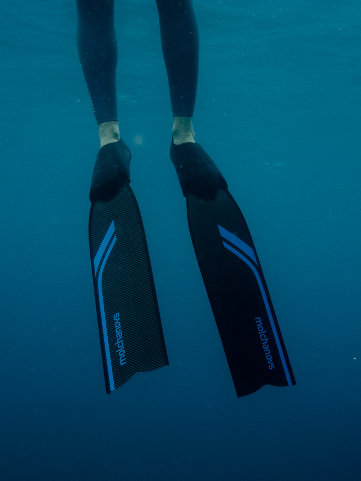Diver's feet wearing Molchanovs SPORT Bifins 3 Carbon fins with blue stripe, shot from below in open ocean