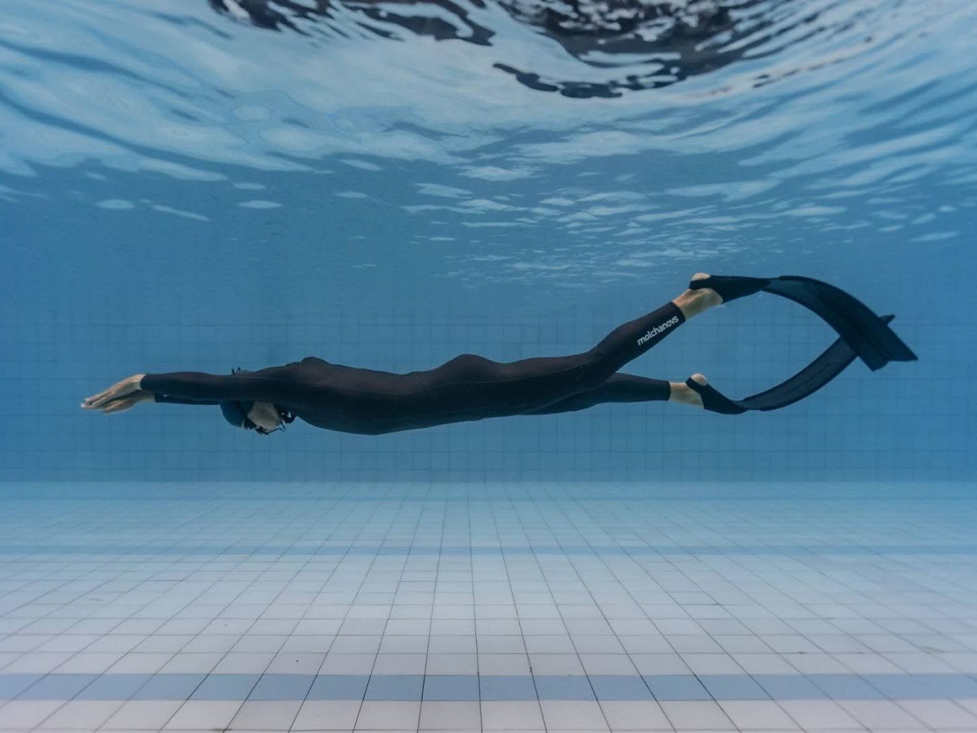 Freediver in black wetsuit using Molchanovs bifins swimming horizontally in a pool